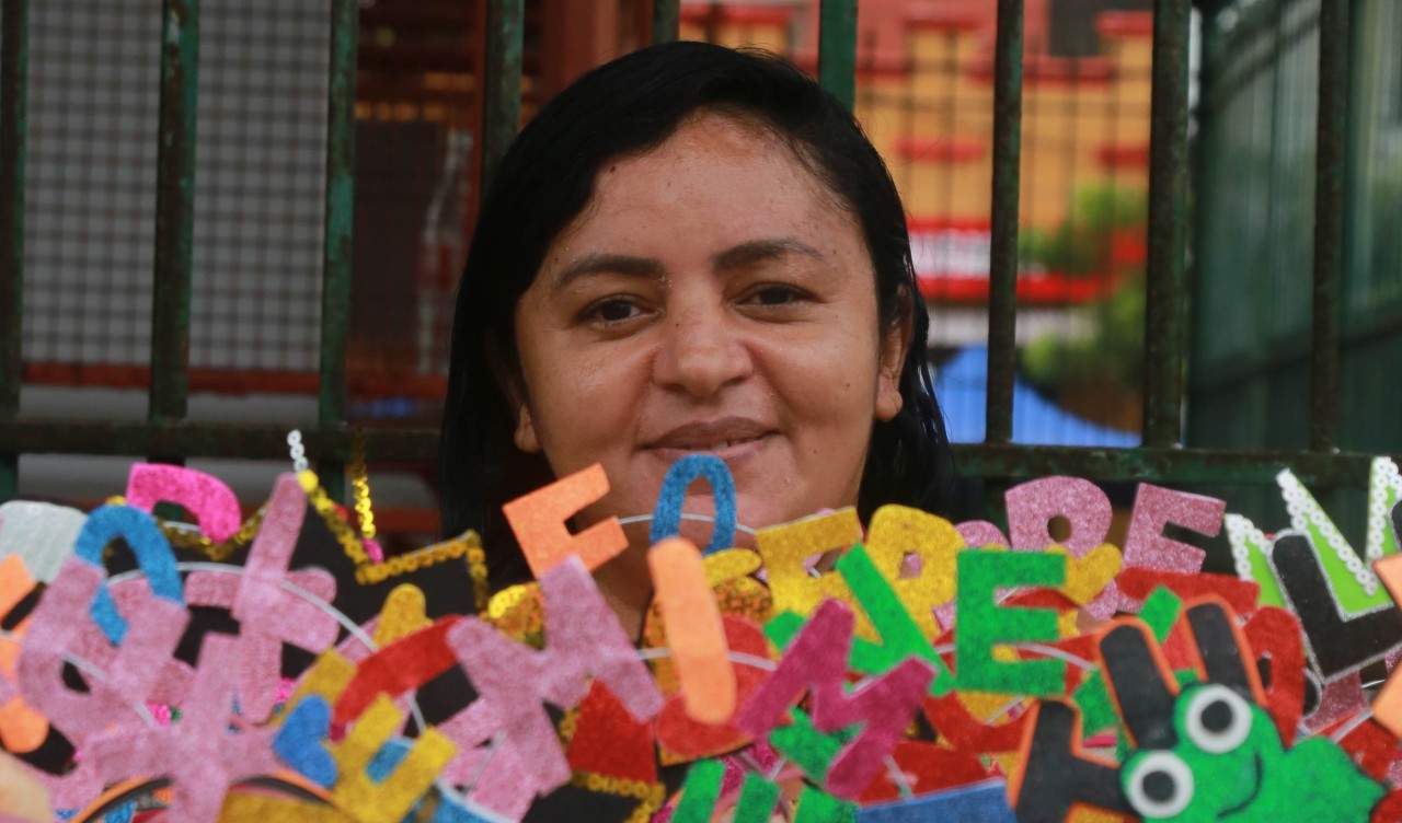 Maria de Fatima Maria enquanto mostra uma tábua de isopor abarrotada de adereços de cabeça com expressões como